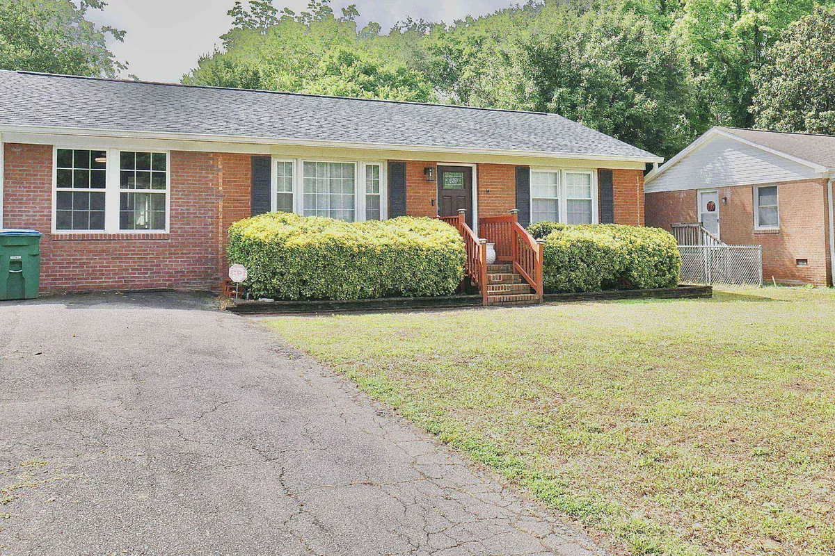 A welcoming view of the home's brick exterior with a lush, green front yard, a cozy front porch, and a driveway. The setting evokes a sense of a peaceful neighborhood, offering additional outdoor space for relaxation or social moments, and hints at the inviting community context described in the section.
