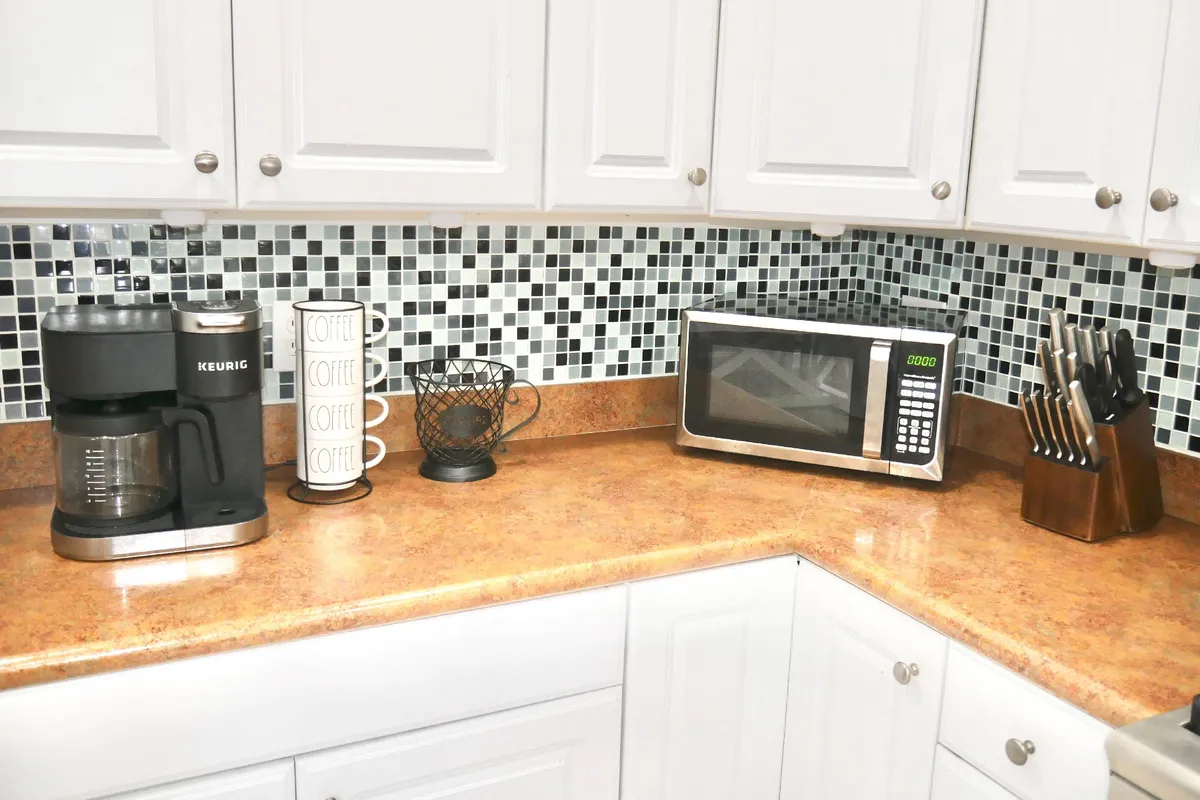 The kitchen area features a coffee maker, microwave, and coffee mugs, evoking a sense of morning routines and casual conversation. The space is cozy and welcoming, ideal for starting the day with a fresh brew or enjoying a quick meal between work sessions.