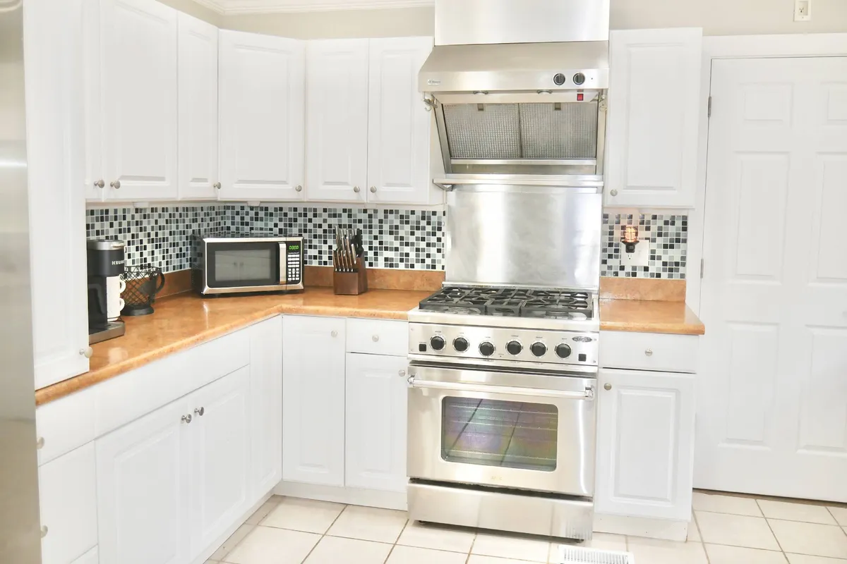 A close-up view of the kitchen’s stainless steel stove, eye-catching colorful backsplash, and granite countertop, highlighting areas used for cooking and baking. The scene feels welcoming and offers a sense of the kitchen’s modern finishes and practical layout.