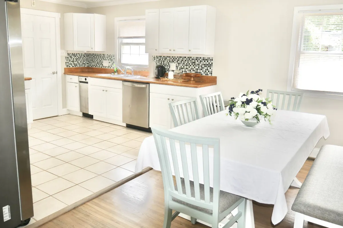 An inviting shot of the dining table adorned with fresh flowers, adjacent to the kitchen’s countertops, visible appliances, and white cabinets. The scene suggests an environment where family meals and casual gatherings come together seamlessly.