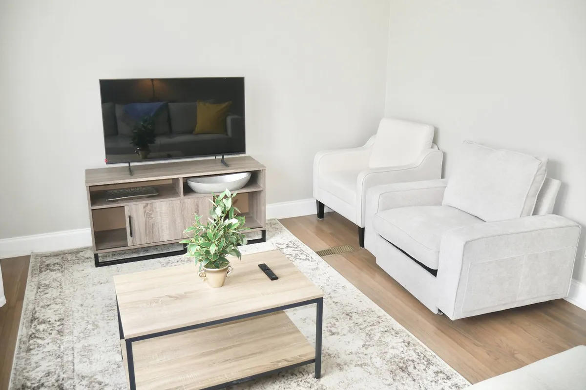 A cozy living area with a television, coffee table, green plant, and armchair. The space is arranged for relaxation, socializing, or catching up on your favorite shows with friends after a day out.