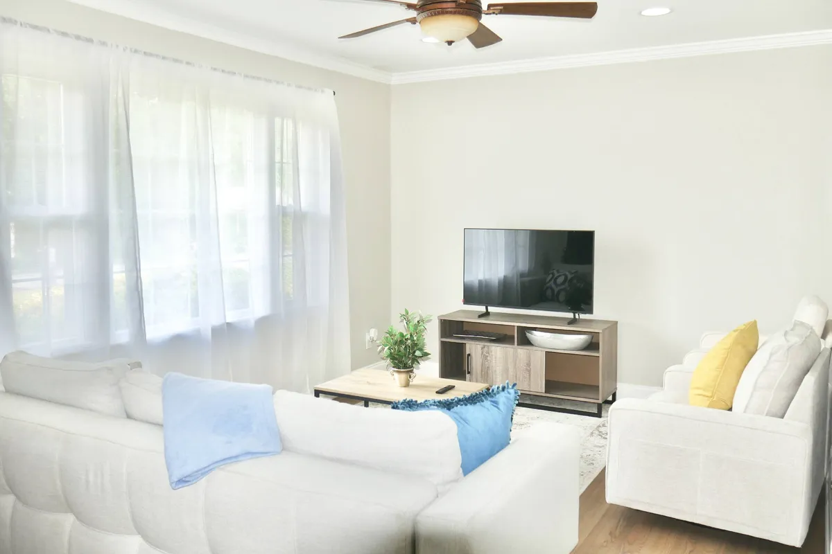 A cozy, open living area featuring a comfortable sofa facing a television, with a coffee table and ceiling fan overhead. The layout is uncluttered, inviting, and set up for both relaxation and socializing.