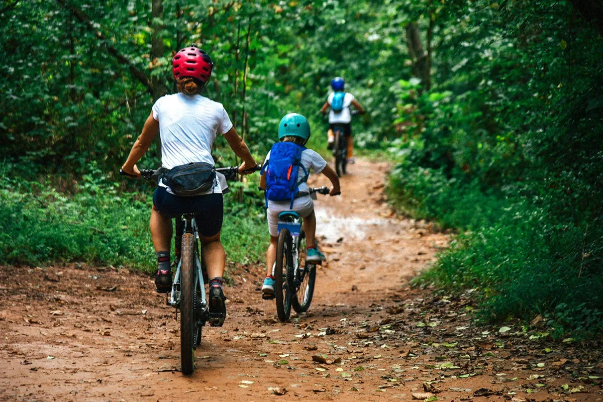 A family bikes together along a lush, tree-lined path, surrounded by vibrant greenery. The image captures the spirit of outdoor adventure and shared experiences in nature.